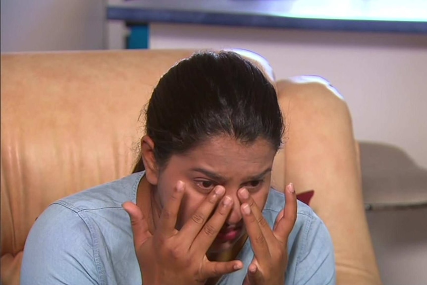 A woman in a blue shirt cries while sitting on a leather couch.