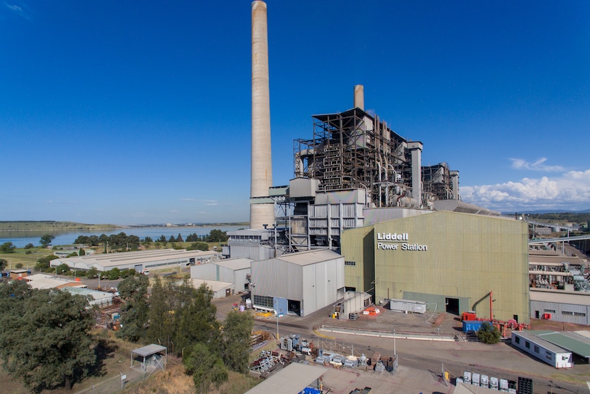 A large green shed that reads 'Liddell Power Station'. Behind it stands two tall power plant stacks and more infrastructure.