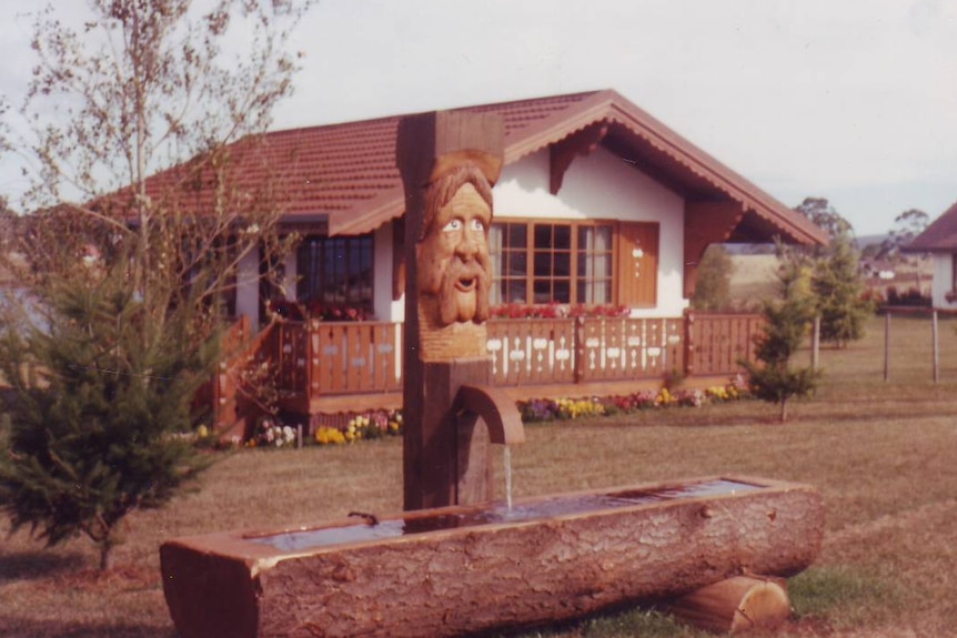 A face carved in wood with a Swiss-styled house in the background