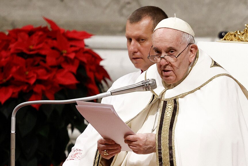 Pope Francis delivers his Christmas address into a microphone while holding sheets of paper