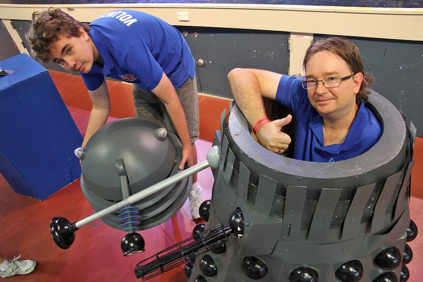 A man inside a dalek suit with the head taken off, gives the thumbs up sign