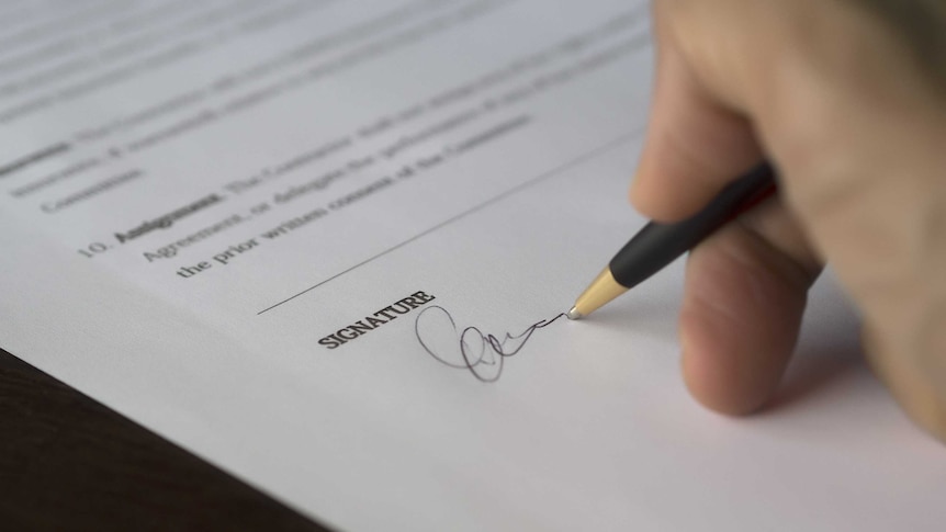 A hand signs a signature with a pen at the end of a form or contract.