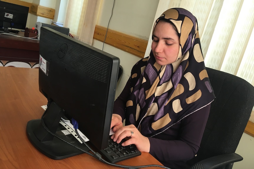 A woman wearing a headscarf types at a computer.