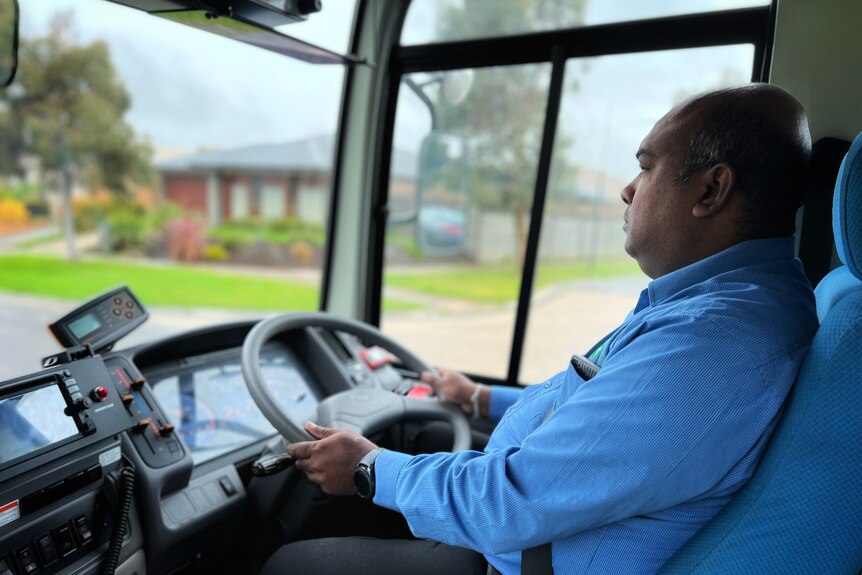 Don Dissanayake sits in the driver's seat of a bus.