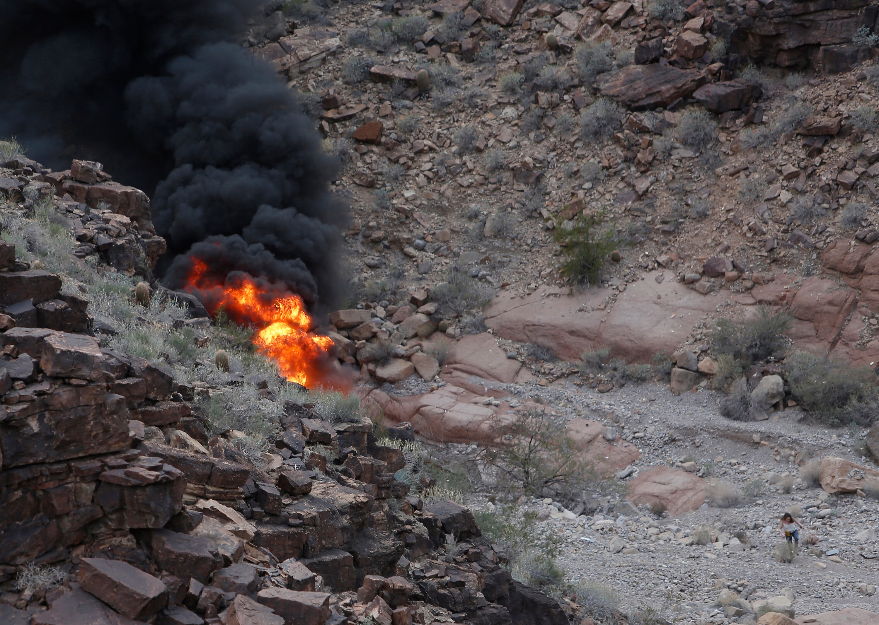 Thick clouds of black smoke and a giant orange and yellow flame and rocks surrounding it.