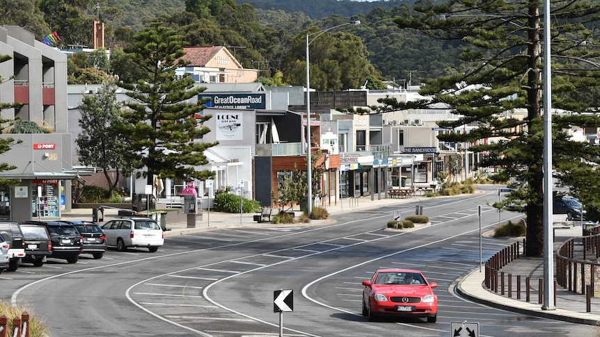 A car drives along a beach-side road lined with shops. 