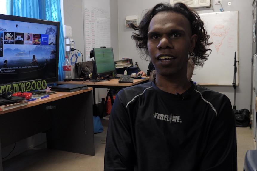 Un joven aborigen con una camiseta negra mira a la cámara.