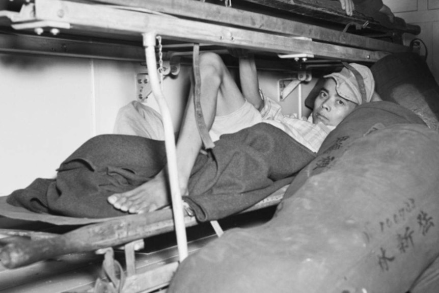 A Japanese prisoner lies under a blanket in an ambulance.