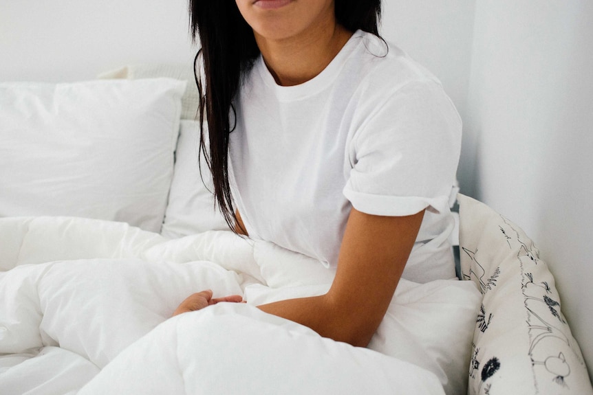Woman wearing a white T-shirt sitting on a bed with white linen