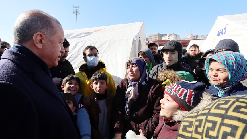 Turkish president speaks to victims of a deadly earthquakes, with temporary shelter tents seen behind them.