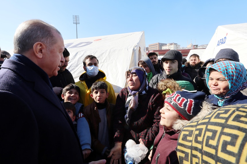 Turkish president speaks to victims of a deadly earthquakes, with temporary shelter tents seen behind them.