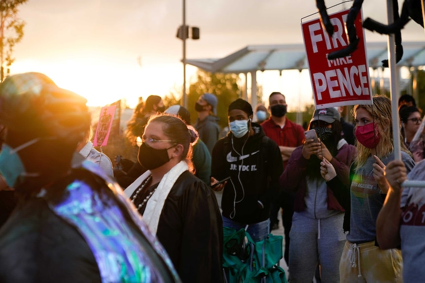 A line of people in face masks as the sun sets