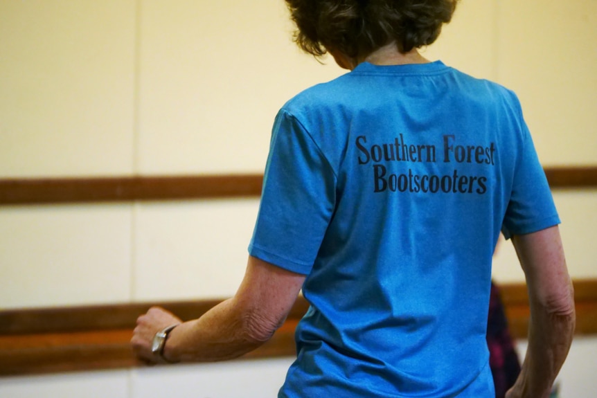 A woman in a blue shirt dances with her back to the camera. Southern Forest Bootscooters written on back.
