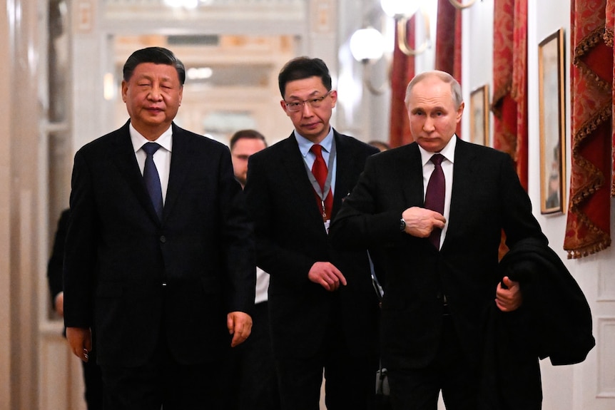 Xi Jinping and Vladimir Putin walk down a hallway in the Kremlin.