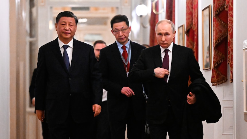 Xi Jinping and Vladimir Putin walk down a hallway in the Kremlin.