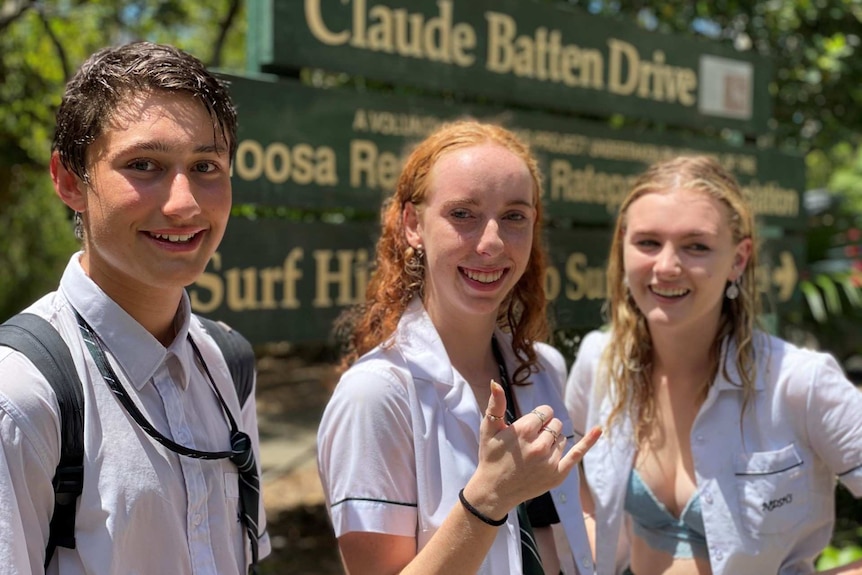 Three teenagers smile in school uniform.