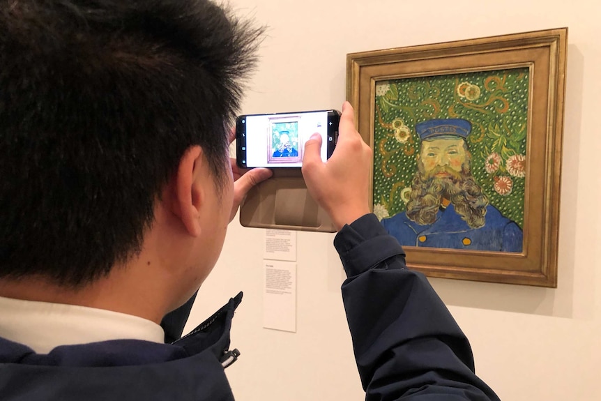 A man takes a photo of a painting on display at the National Gallery of Victoria.