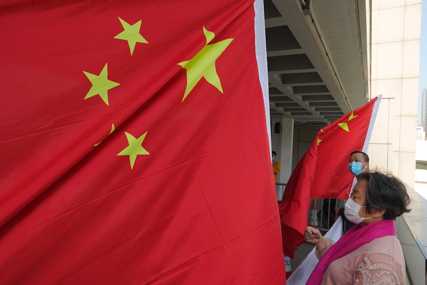 Pro-China supporters wearing disposable face masks as they wave the red and yellow flag of China while standing on a balcony.