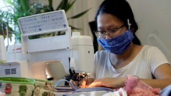 Woman wearing blue mask at sewing machine.