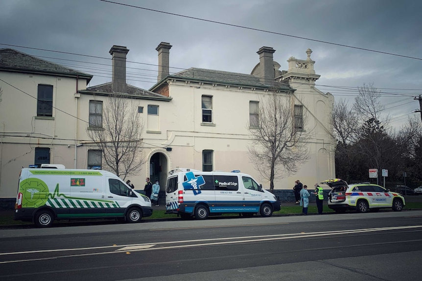 Medical transport vans parked in a street outside a Victorian-era building.