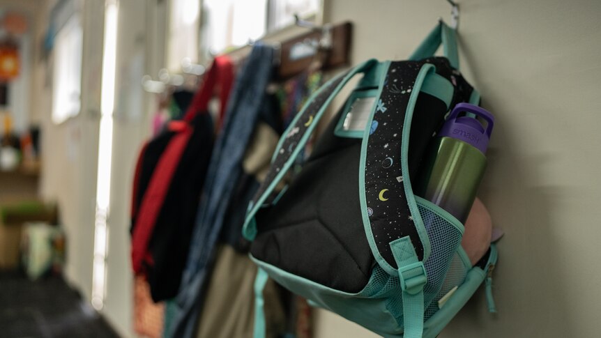 A young child's school bag hangs on a hook in a classroom.