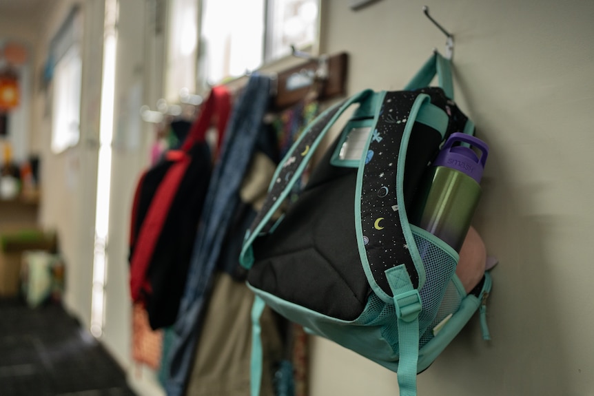 A young child's school bag hangs on a hook in a classroom.