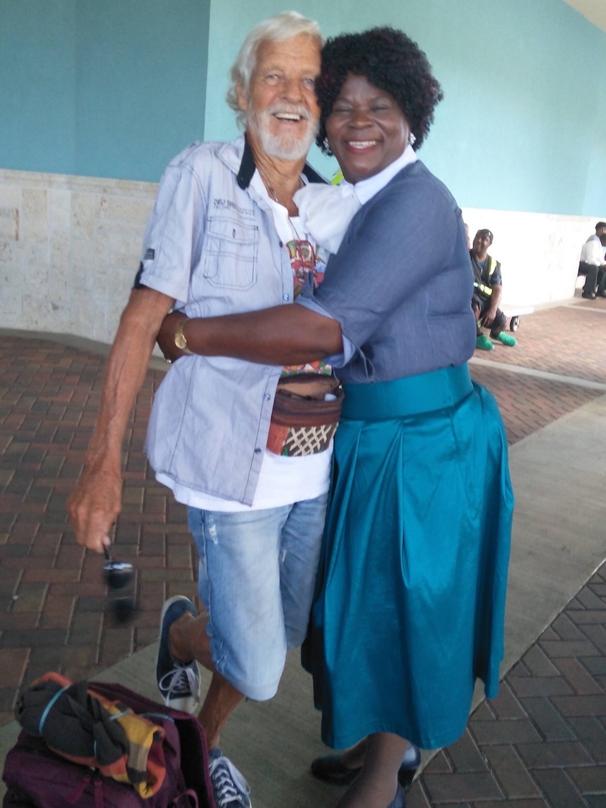 an older man stands with a woman, they are embracing and smiling at the camera
