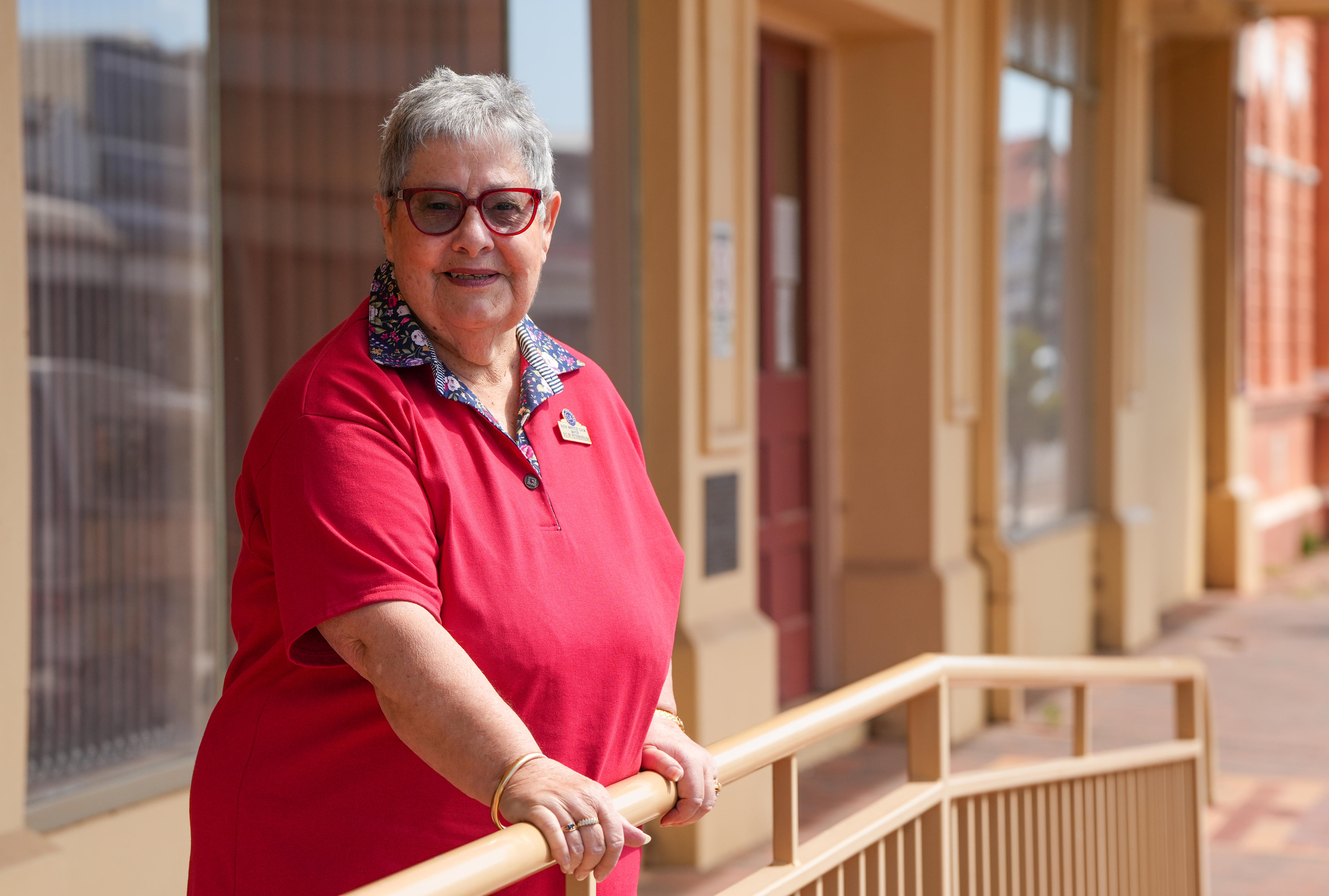Mayor Ruth Whittle of the Peterborough District Council, wearing a red shirt and spectacles, stands outside a building