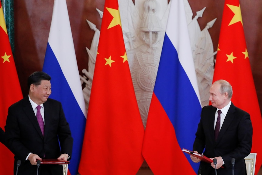 Chinese President Xi next to Russian President Putin with Chinese and Russian flags in background.