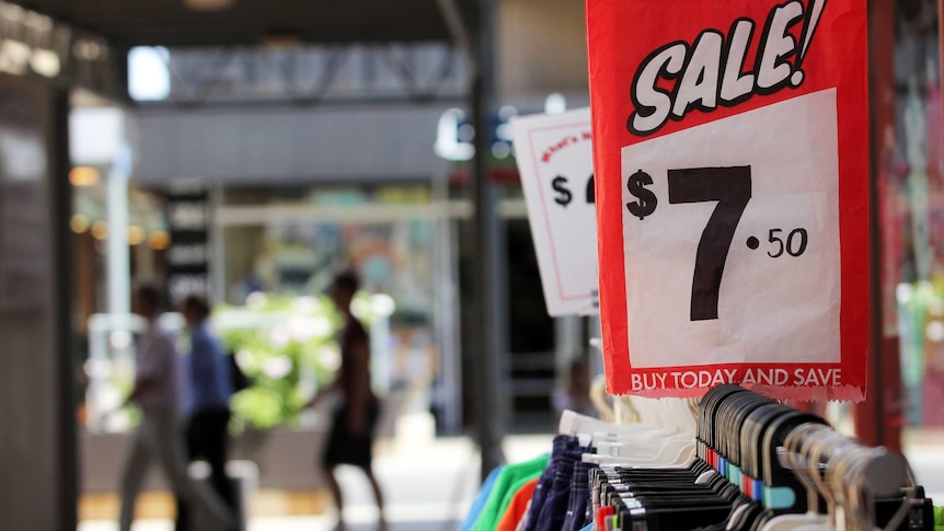 A sale price sign on a rack of clothes outside a shop