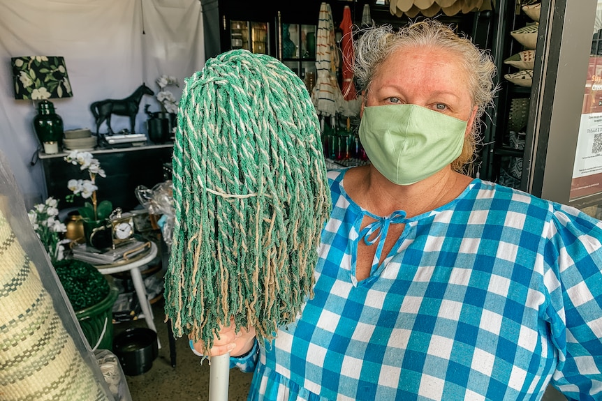 A woman stands in front of a store holding a mop