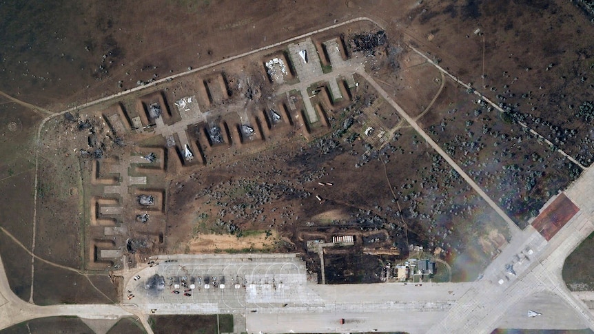 above-ground satellite image of an air base that appears to have been on fire, equipment looks damaged and nearby trees burnt