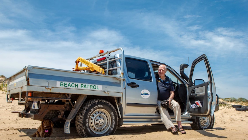 An elderly man sits in his beach patrol ute on the beach