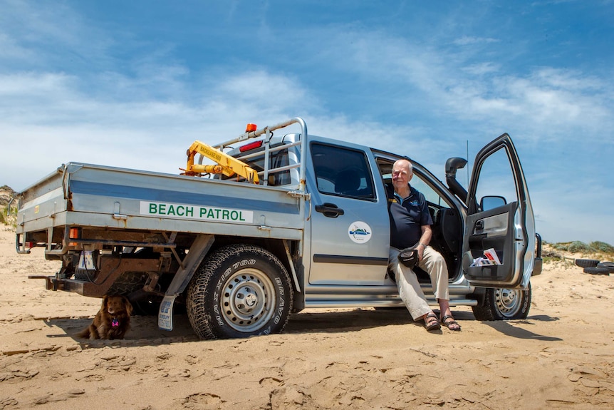 An elderly man sits in his beach patrol ute on the beach