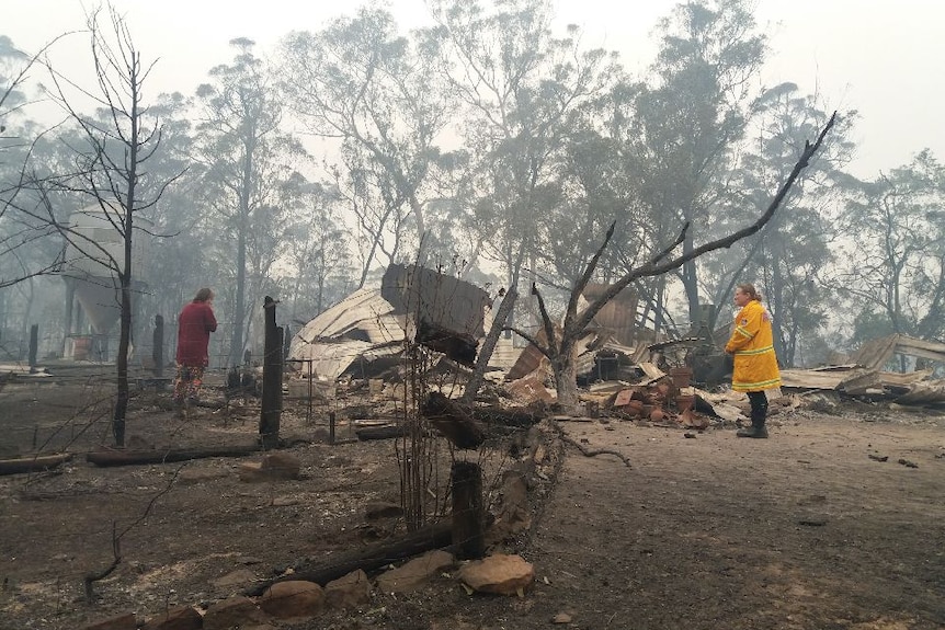 A burnt-out house with a person in a firefighting jacket in the foreground.