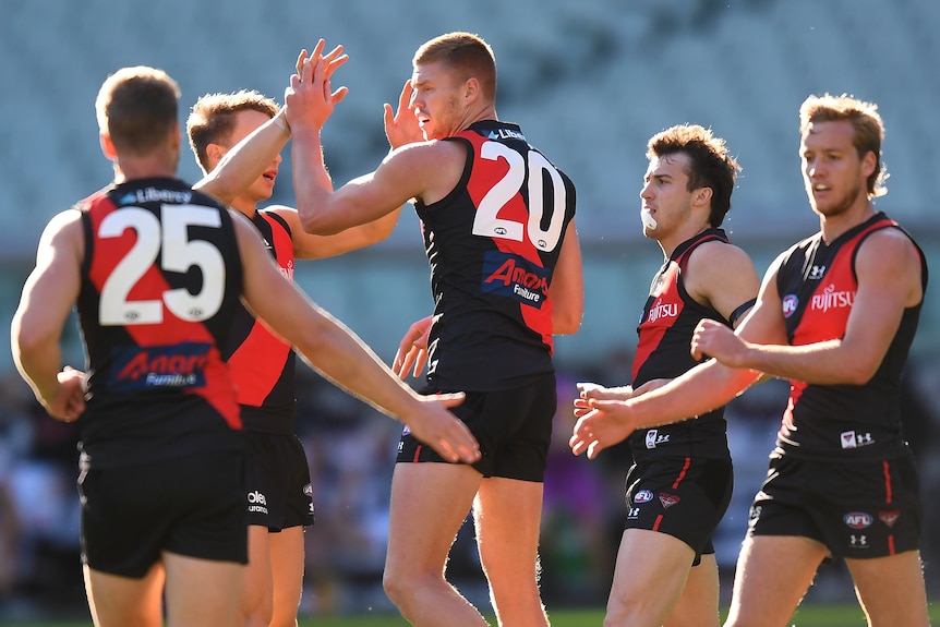 An Essendon forward gets congratulations and pats on the back after kicking a goal. 