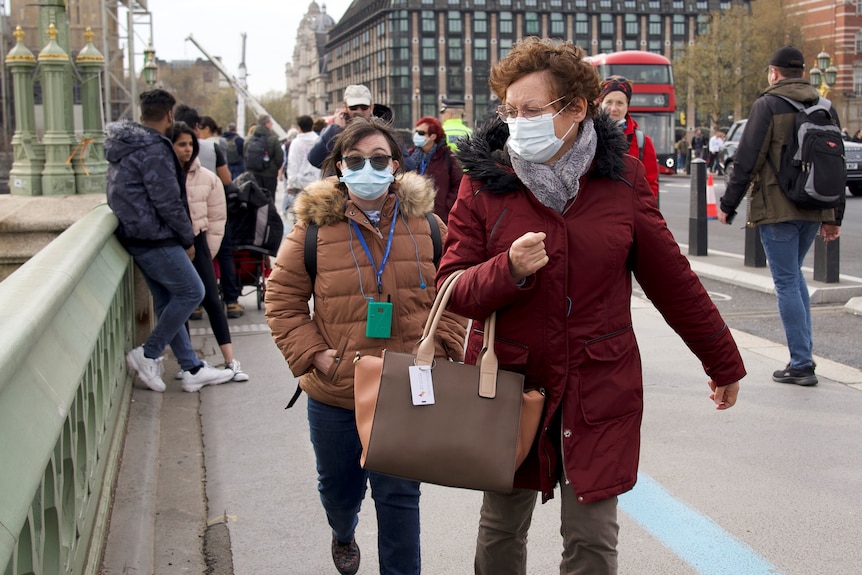 Two women wearing puffer jackets and masks walk on London Bridge.