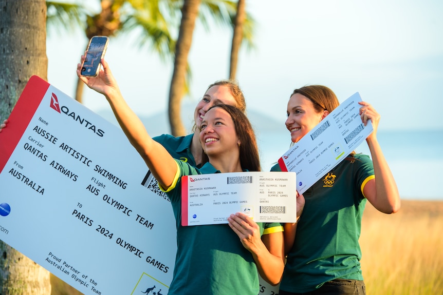 Three swimmers hold oversized plane tickets taking a selfie