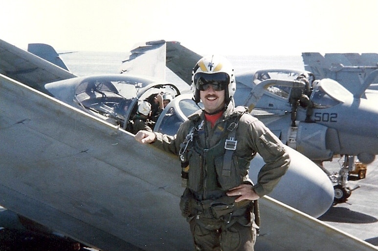 A man in pilot uniform standing next to a plane
