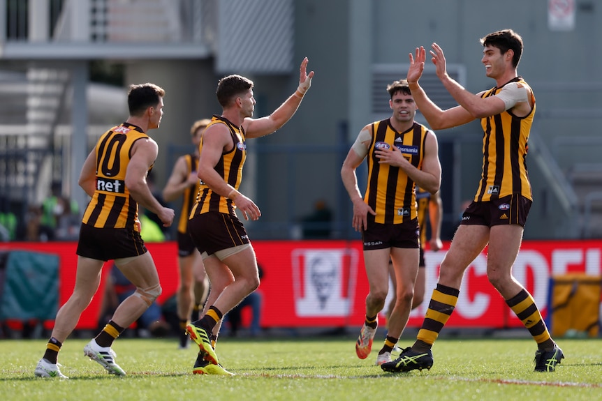 A group of players in yellow and black jerseys congratulate each other in an empty AFL stadium.
