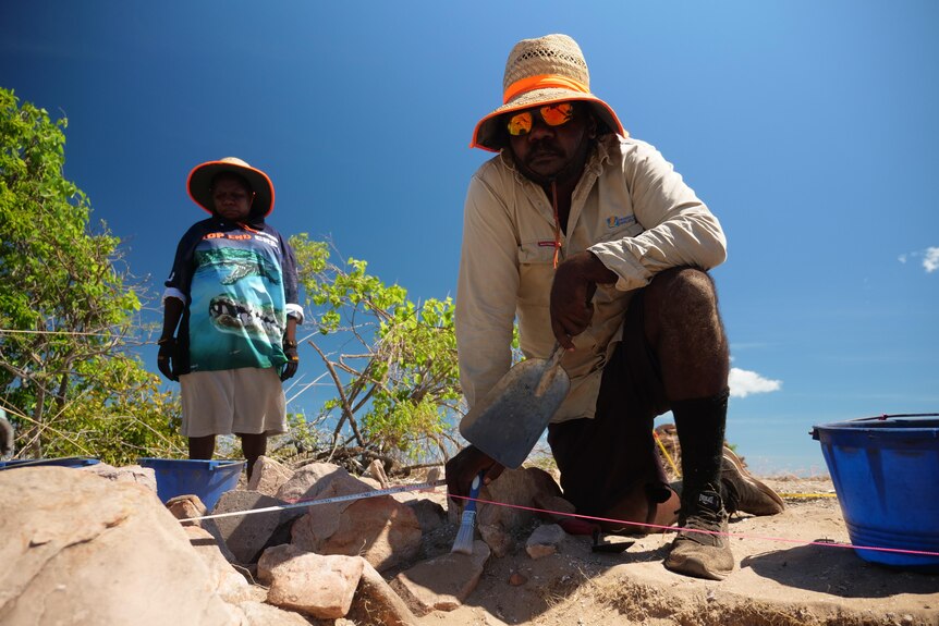 An Aboriginal man kneels at an archaeological dig.