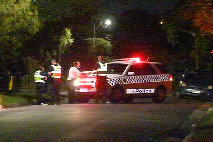 Police officers stand around a police car in a dark street.