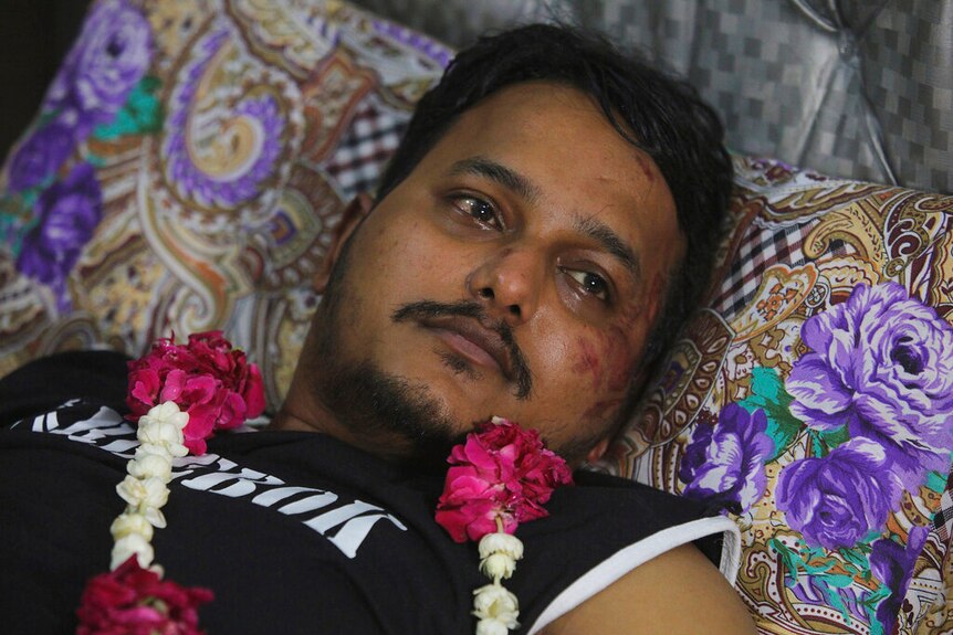 A photo of the survivor in bed with a flower necklace around him, with cuts and bruises on his face.