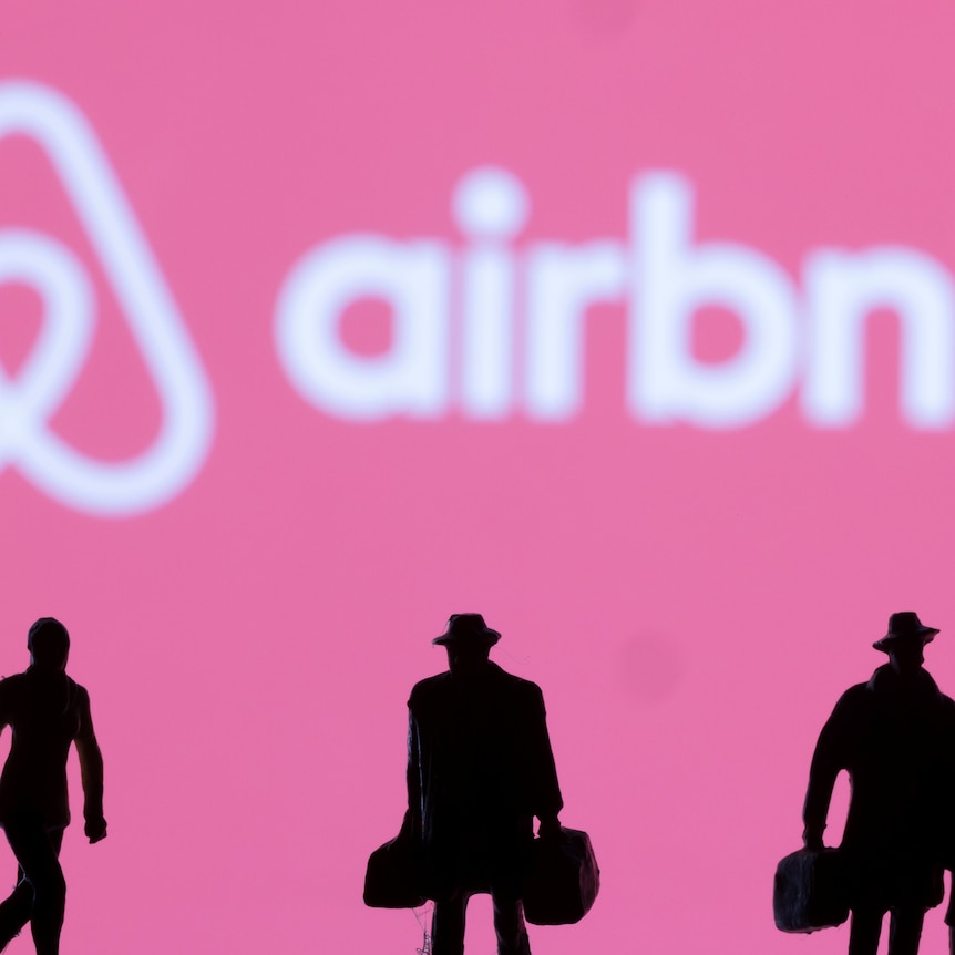 Airbnb logo on a pink background with silhouetted figurines of travellers with bags in the foreground
