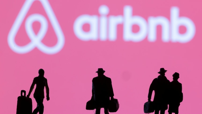 Airbnb logo on a pink background with silhouetted figurines of travellers with bags in the foreground