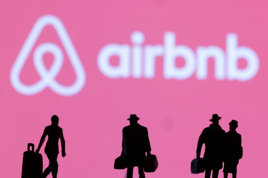 Airbnb logo on a pink background with silhouetted figurines of travellers with bags in the foreground