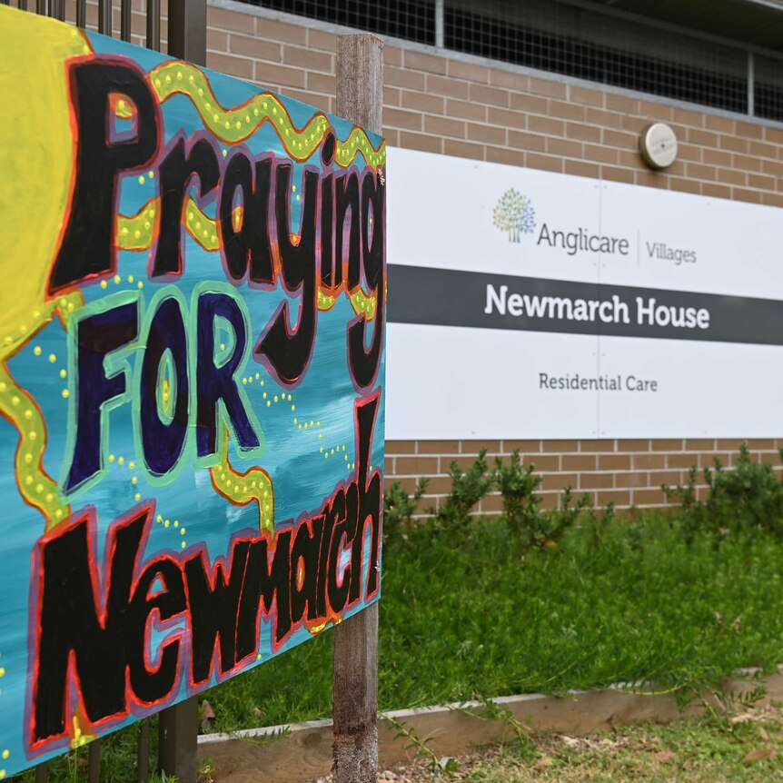 A colourful sign says "Praying FOR Newmarch" outside the front of Newmarch House.