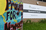 A colourful sign says "Praying FOR Newmarch" outside the front of Newmarch House.