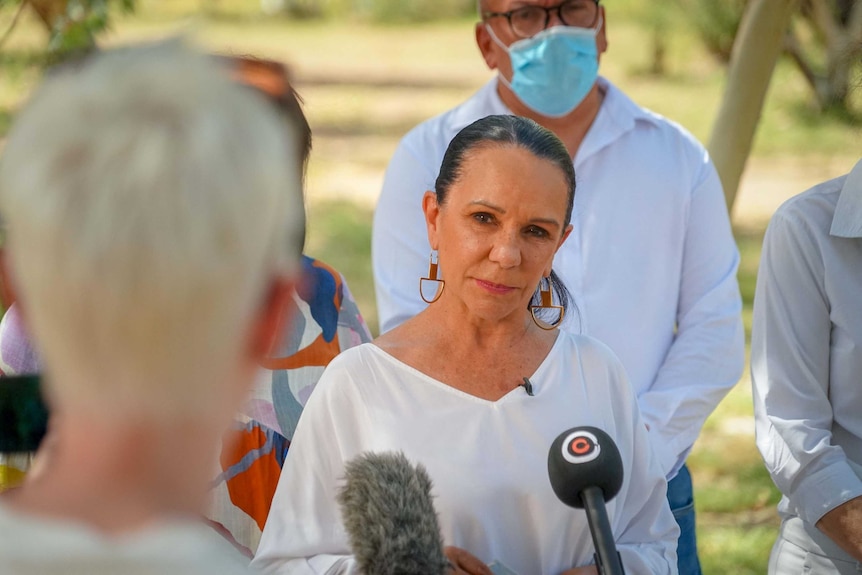 A First Nations woman wearing a white top addresses media at a press conference