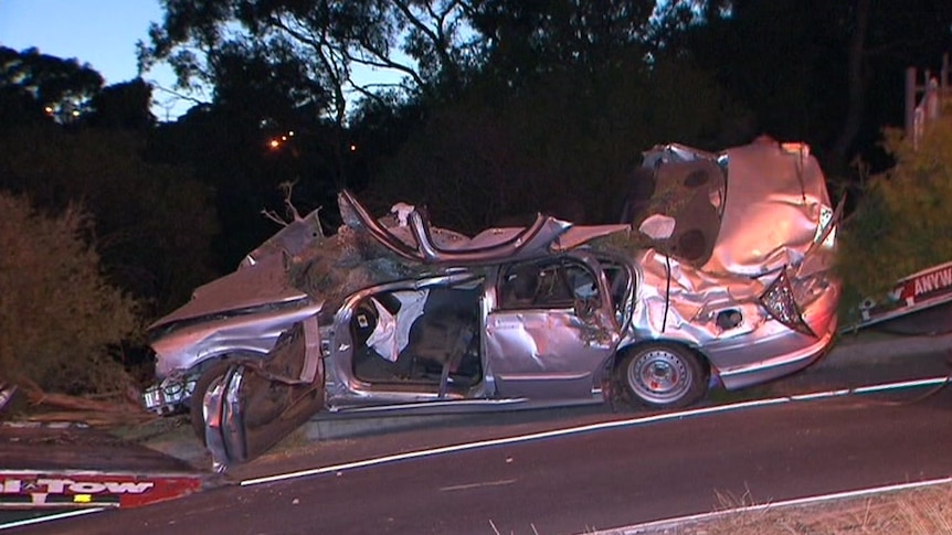 The wreckage of a silver Ford sedan after crashing into trees.